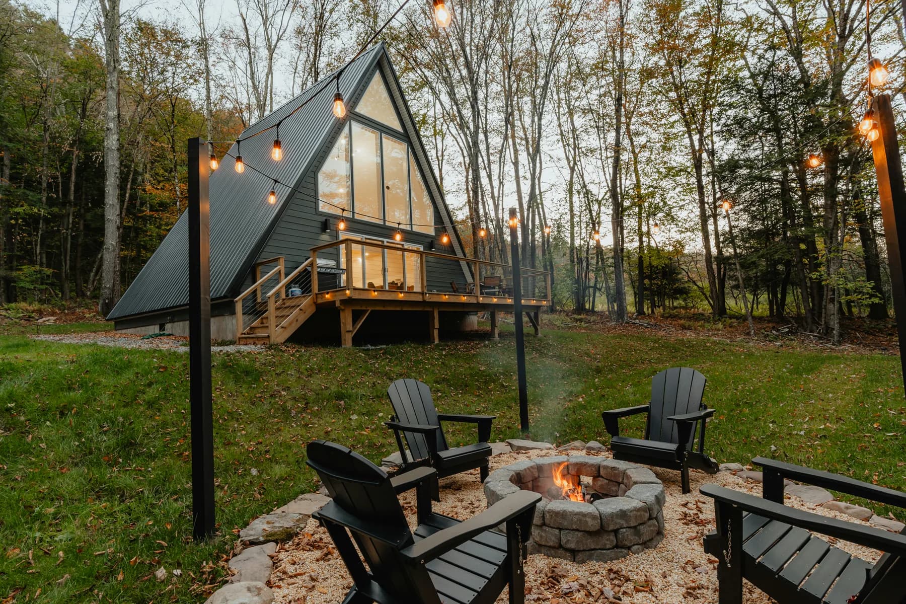 Stone fire pit with flames at dusk beside a modern cabin patio
